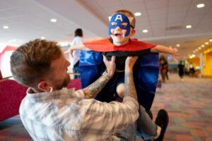 a boy dressed as a superhero pretending to fly while his father holds him up